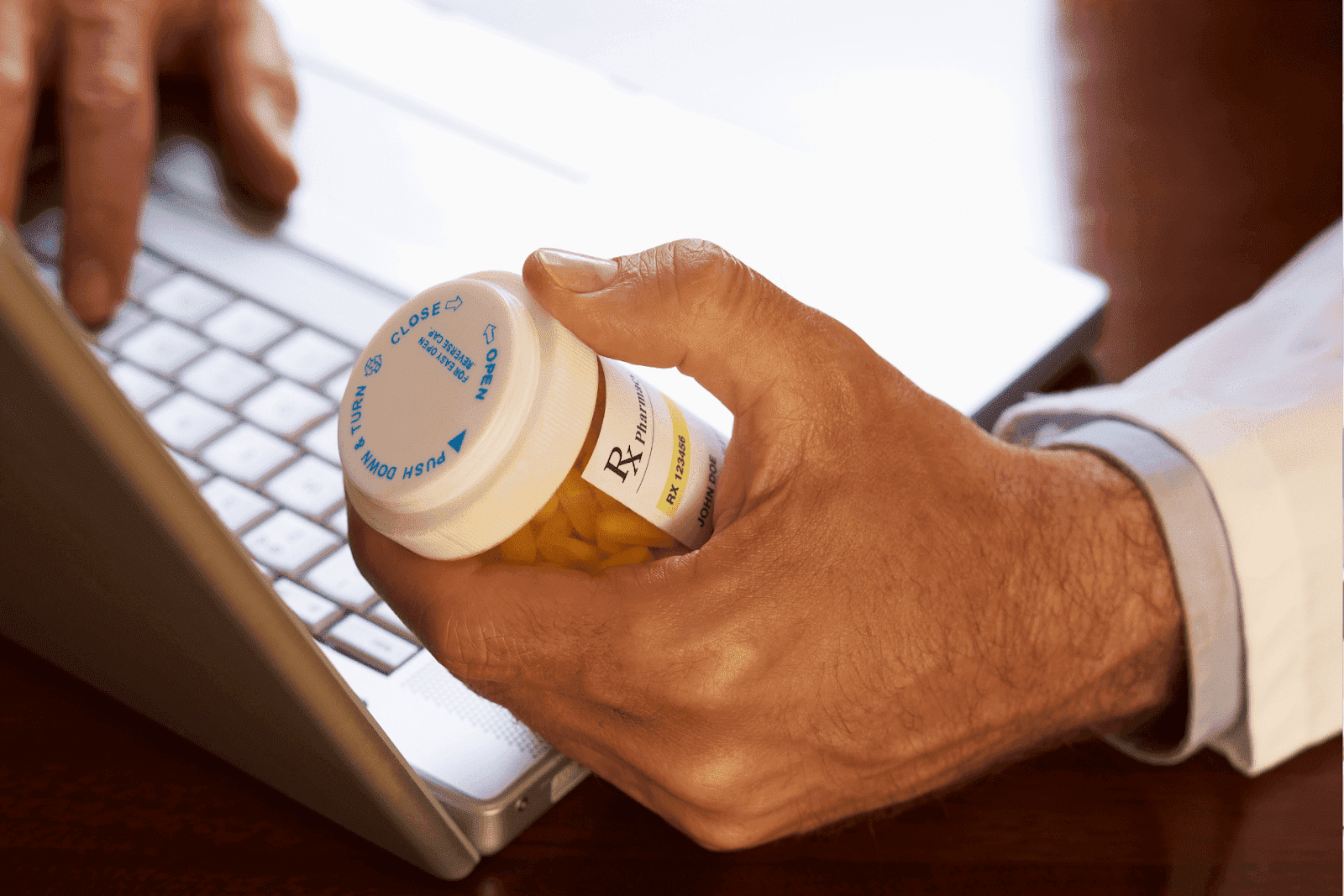 A close-up of a person holding a prescription pill bottle while using a laptop