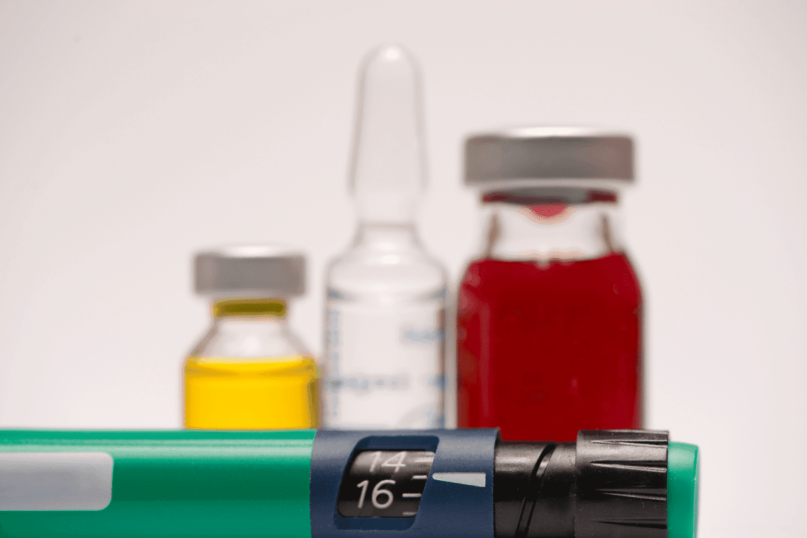 A close-up of an insulin pen with colorful medication vials in the background