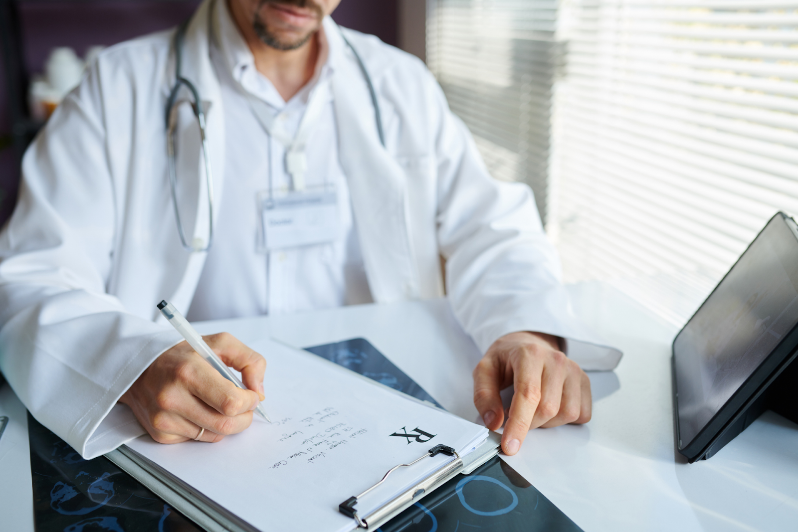 A doctor in a white coat is prescribing a clipboard while pointing at the paper.