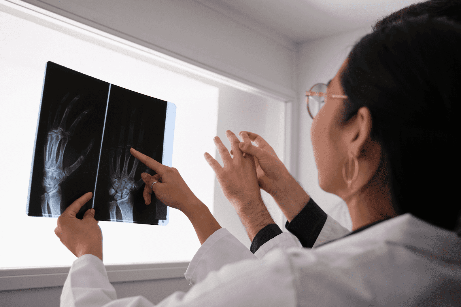 A doctor is reviewing X-ray images of a patient’s hand, closely analyzing the bones and joints