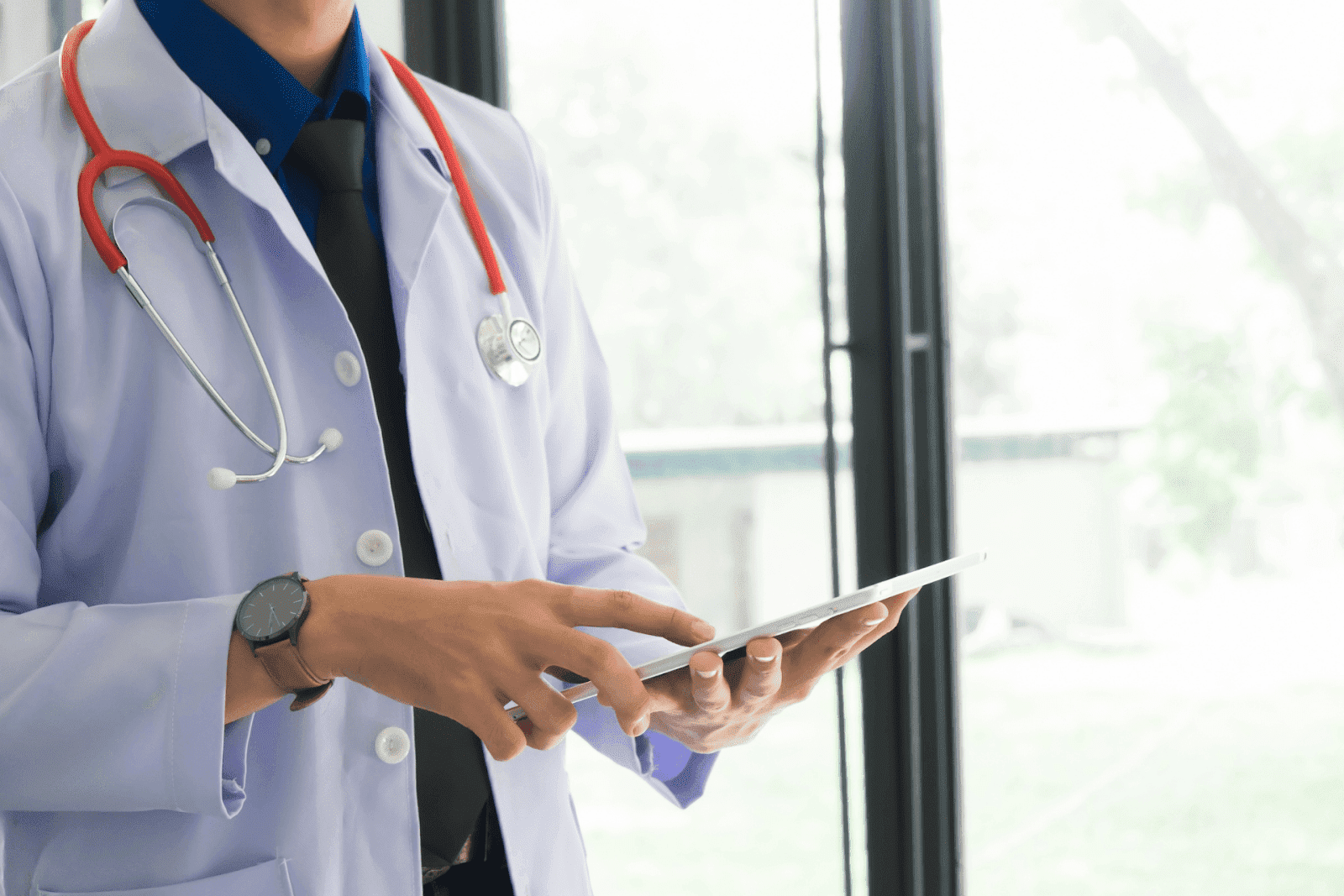 A doctor using a tablet with a stethoscope around their neck
