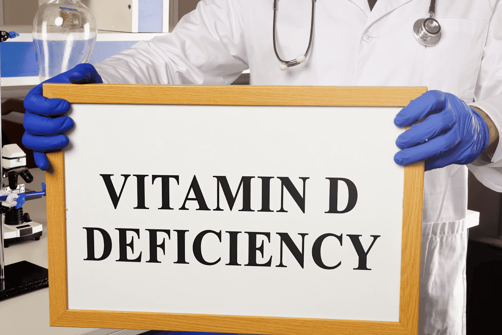 A healthcare professional holding a sign that reads “Vitamin D Deficiency” in a clinical setting.