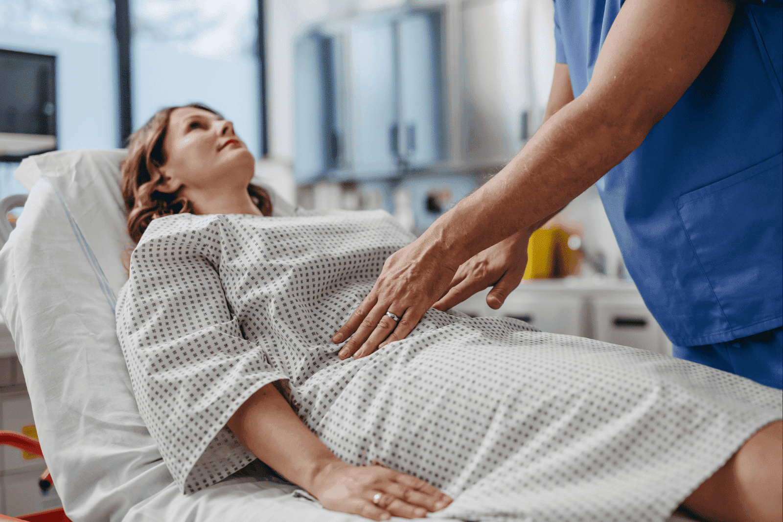 A healthcare professional is performing an abdominal examination on a female patient lying on a hospital bed