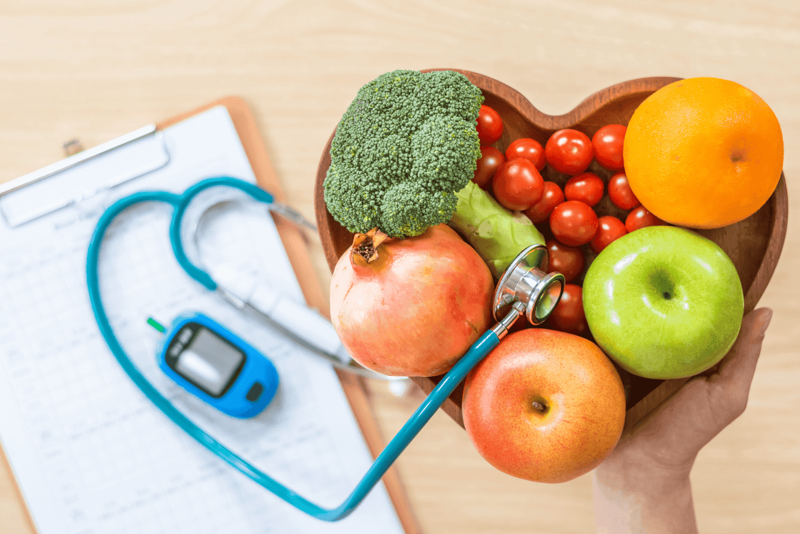 A heart-shaped bowl of fruits and vegetables with a stethoscope and glucometer on a clipboard in the background