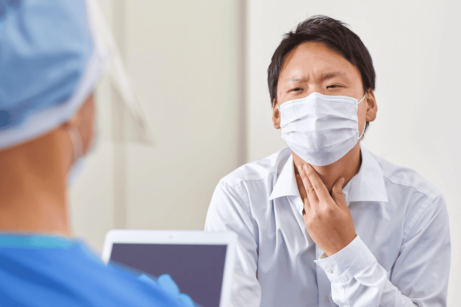 A man wearing a face mask touches his throat while speaking with a healthcare professional.