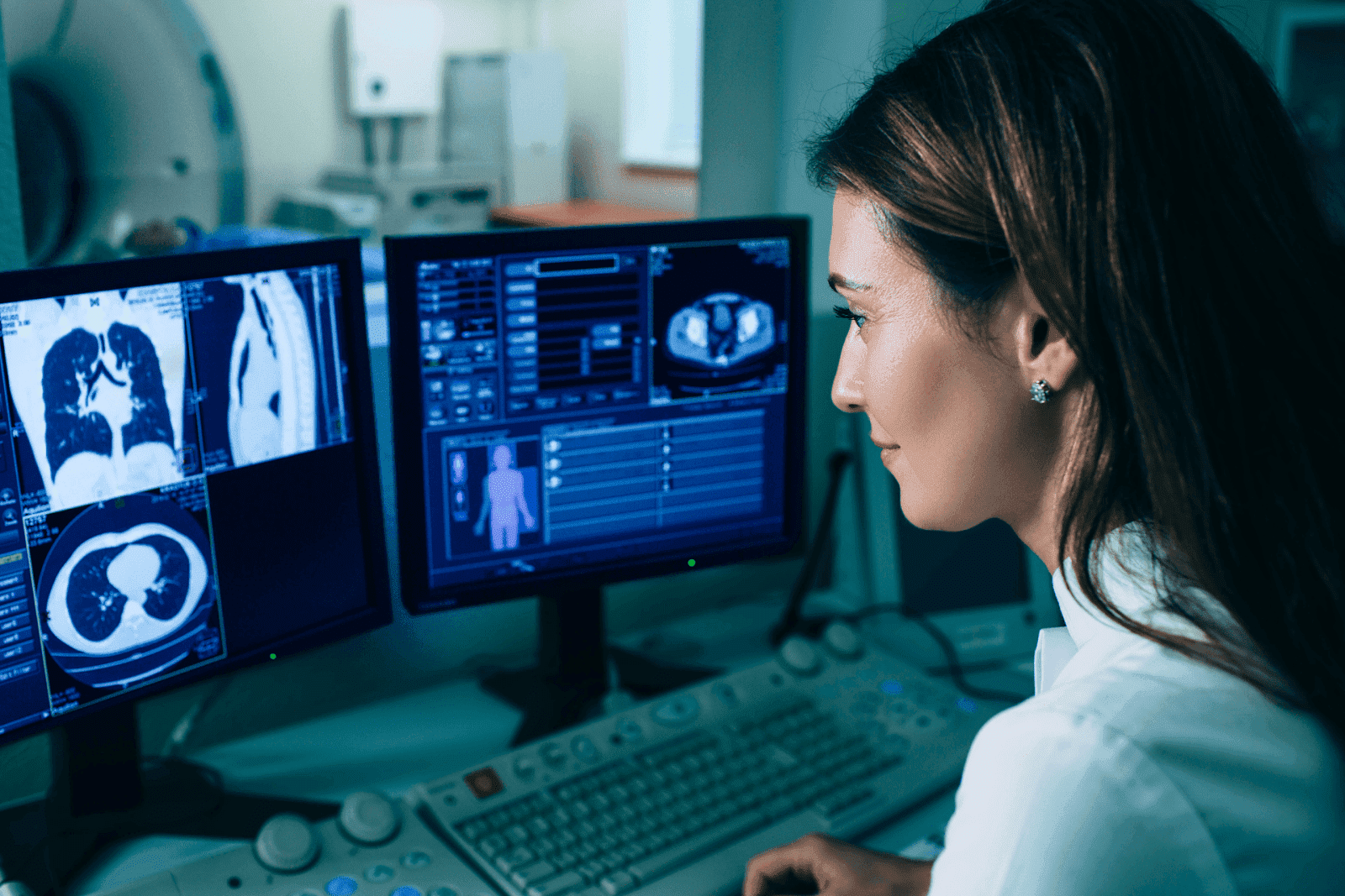 A medical professional examines CT scan images on computer monitors in a radiology lab.