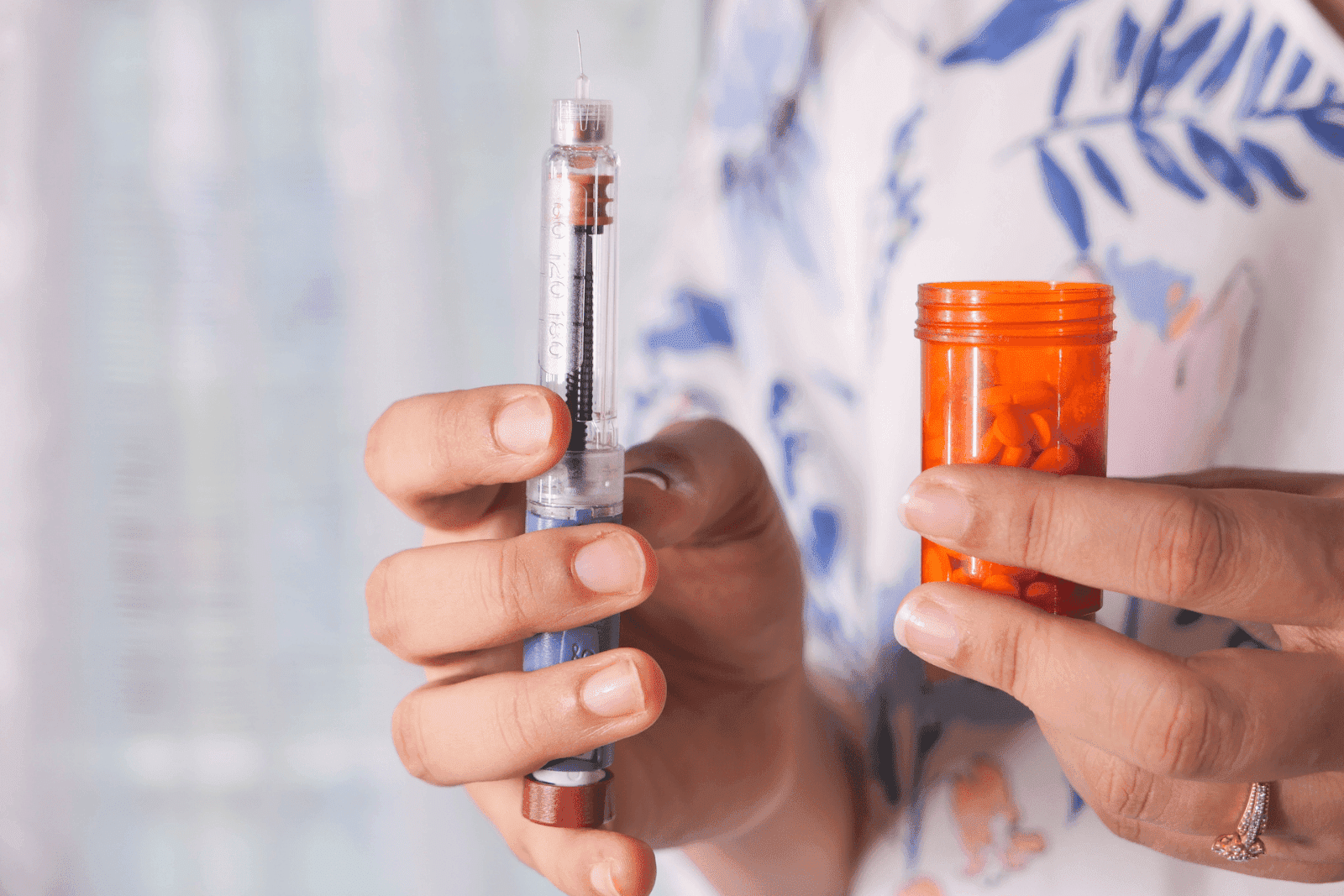 A person holding an insulin pen in one hand and an orange pill bottle in the other