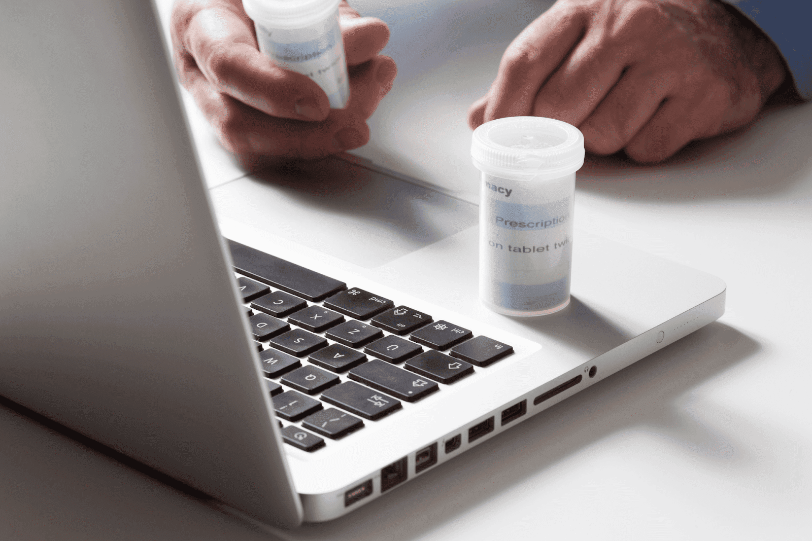 A person holding prescription pill bottles near a laptop