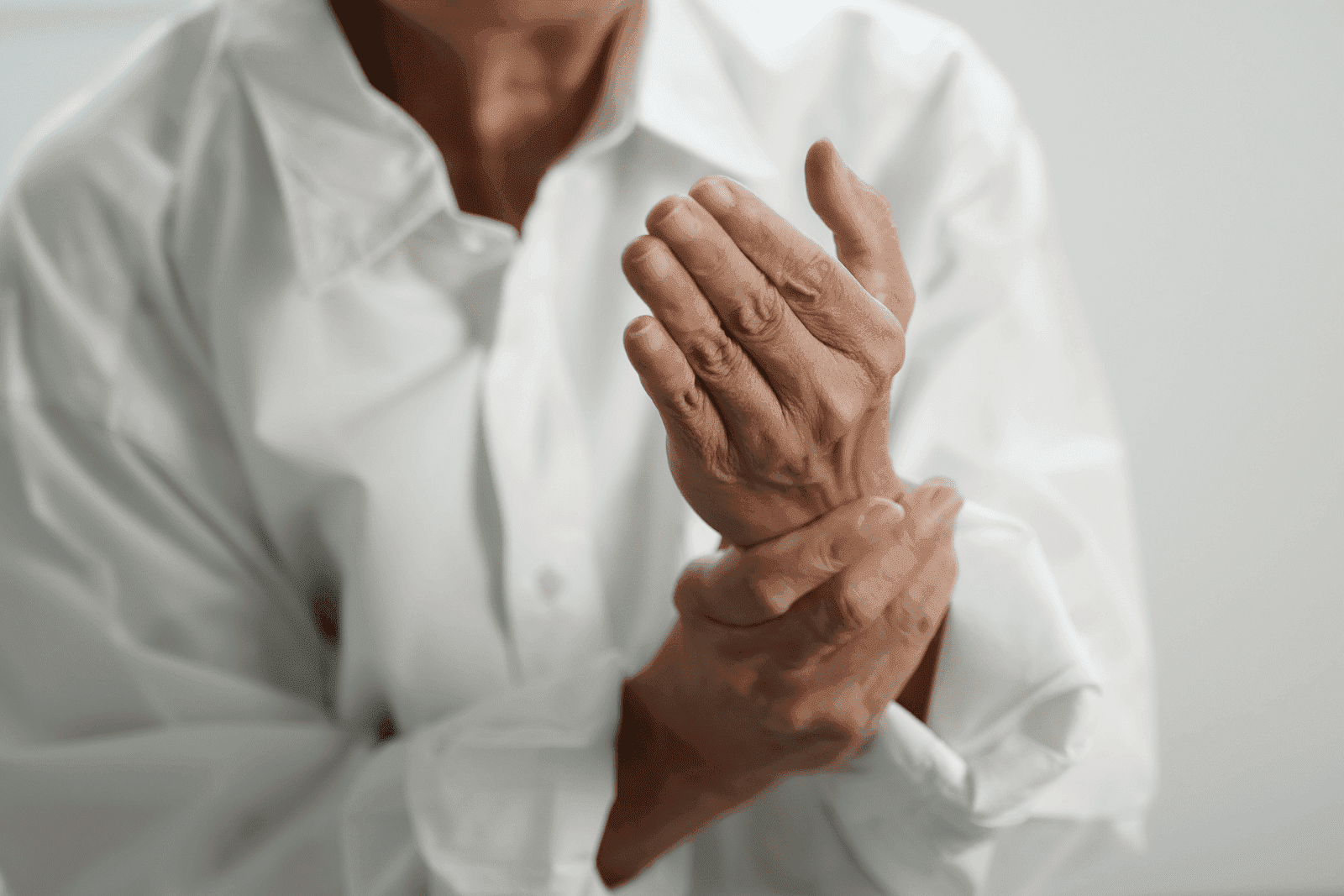 A person is holding their wrist and hand in discomfort, showing visible signs of pain