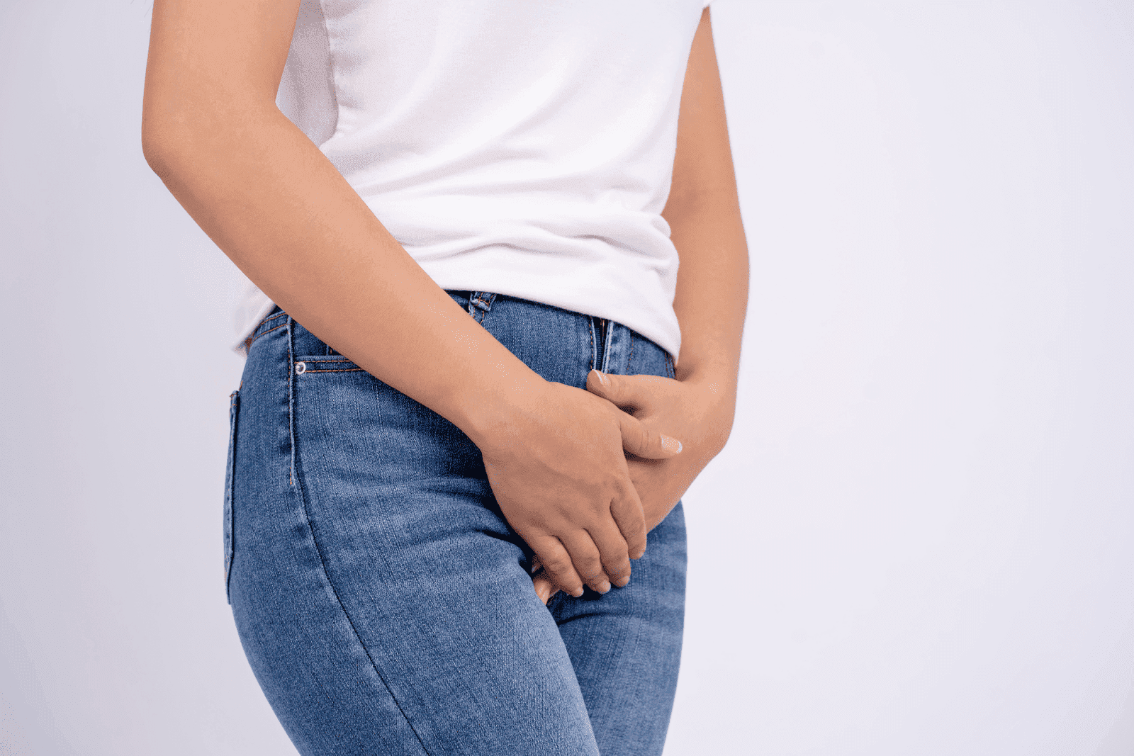 A person standing with hands clasped over their groin area, suggesting pelvic or urinary discomfort.