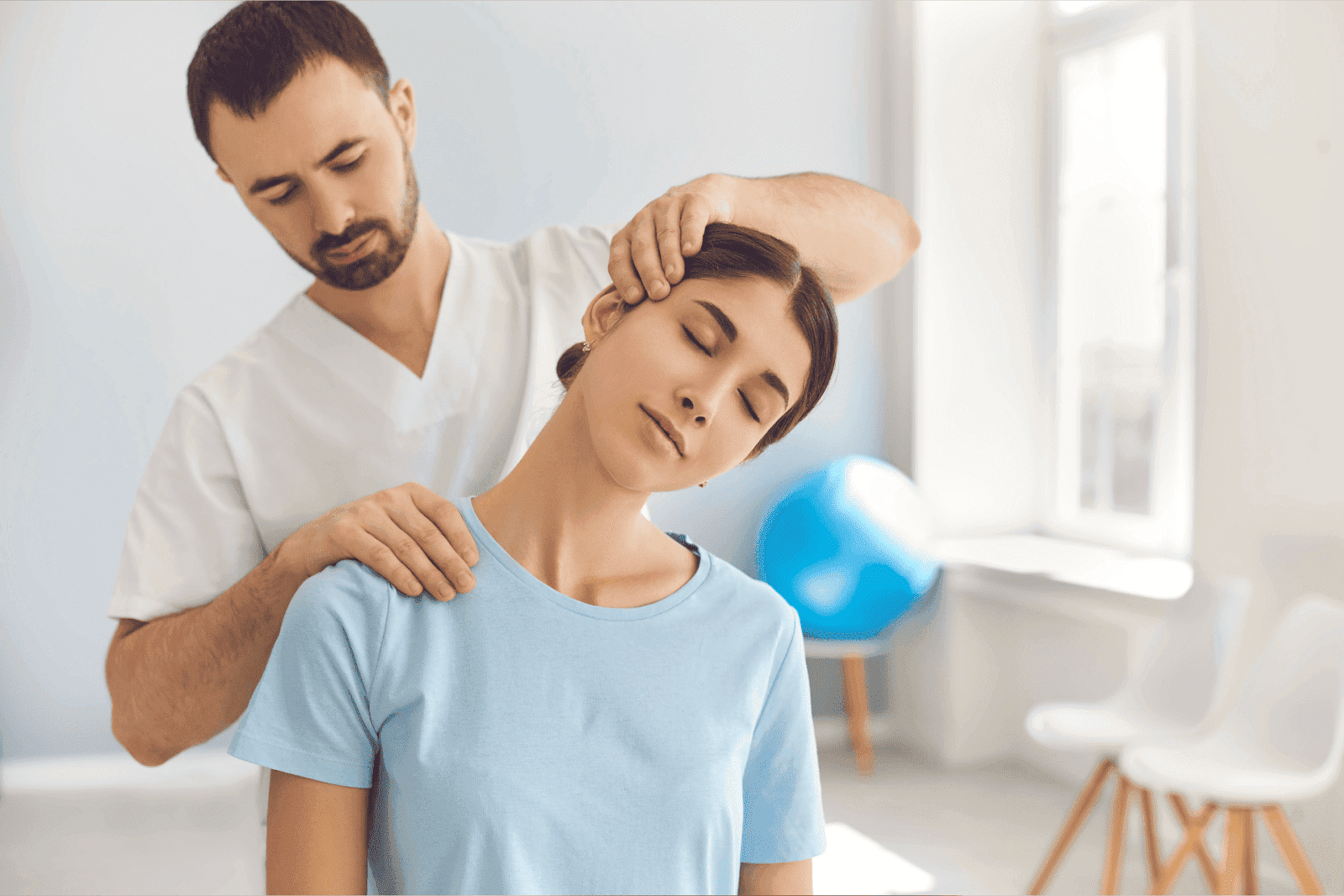 A physical therapist in a white uniform gently stretches a woman’s neck