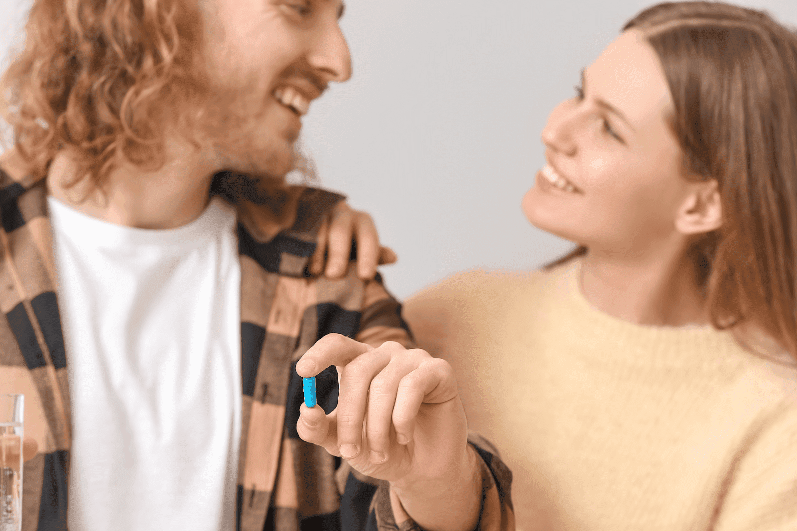 A smiling couple looks at each other as the man holds a blue pill in his hand