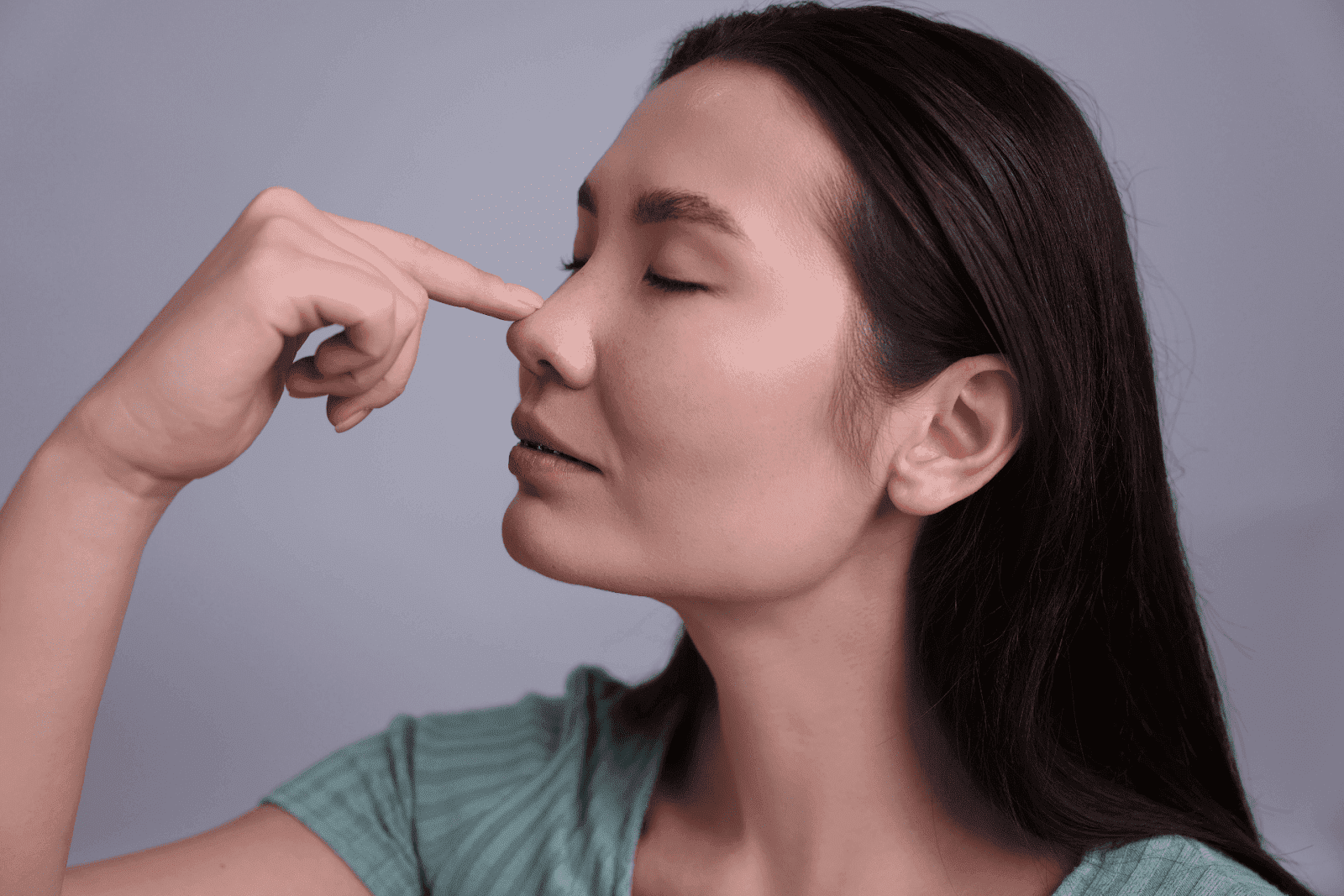 A woman closing her eyes while pinching her nose.