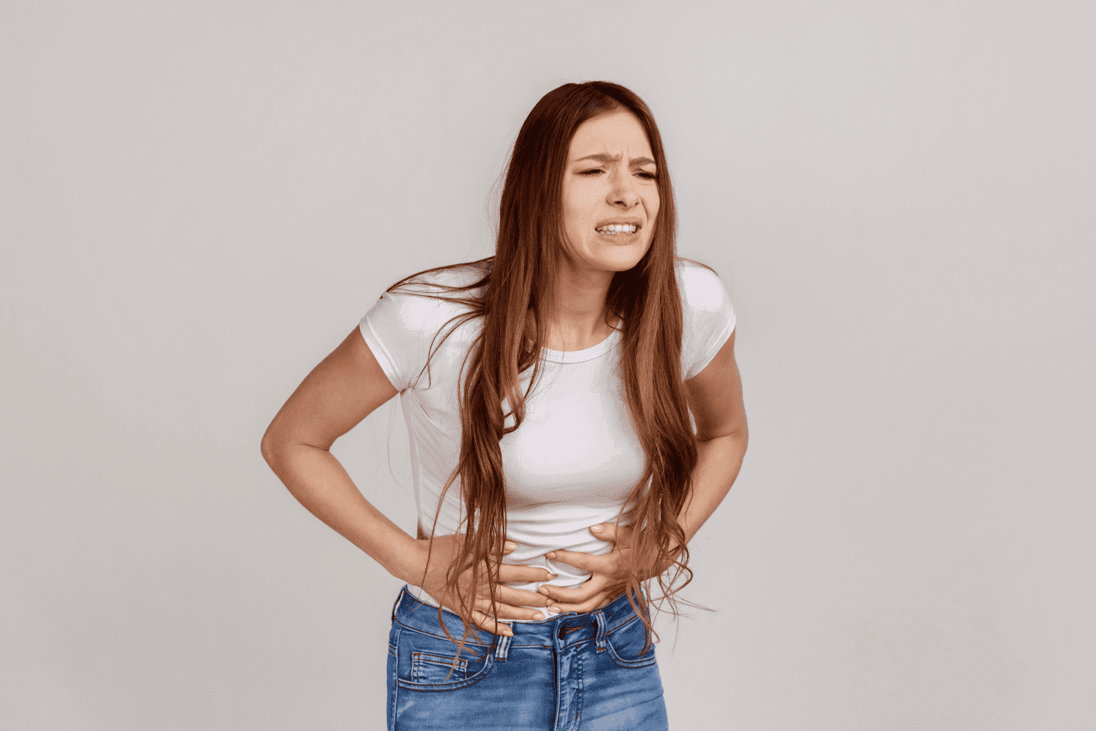 A woman in a white t-shirt and jeans holding her lower abdomen