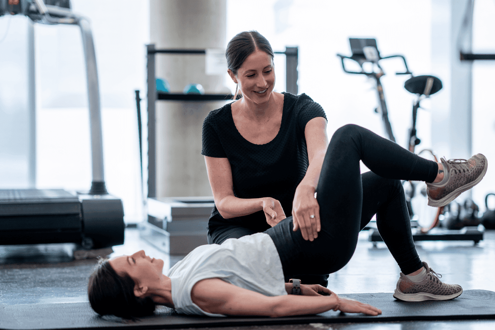 A woman is performing a pelvic floor exercise on a mat while being guided by a therapist