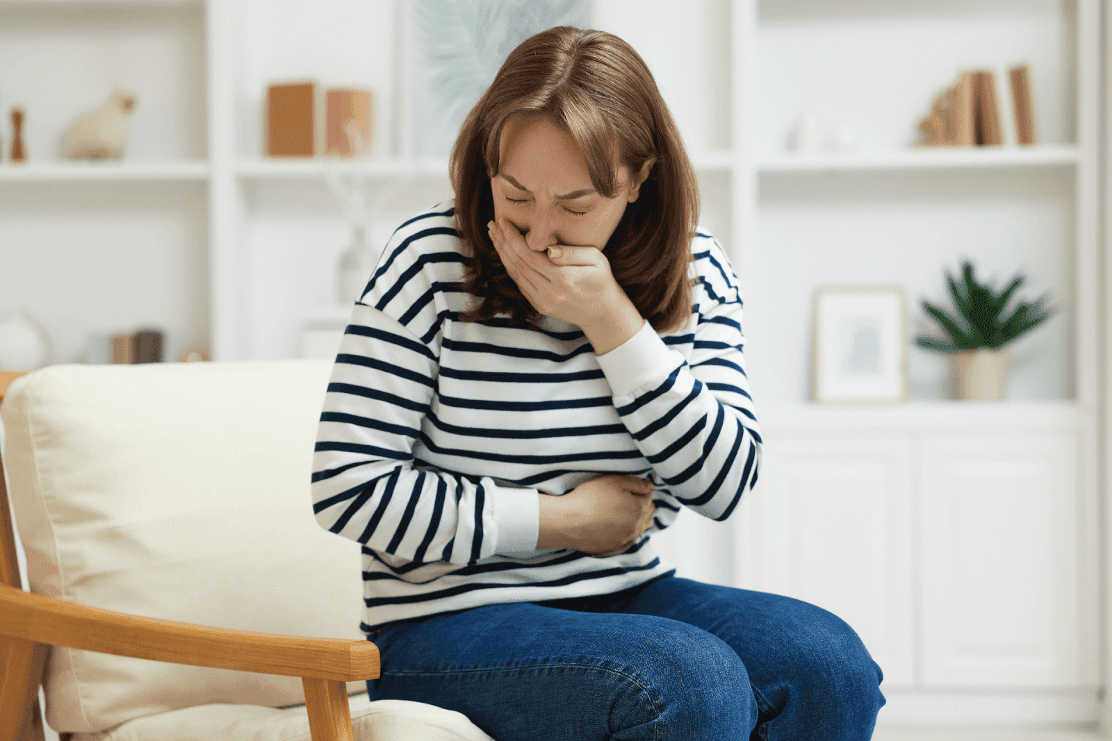 A woman sitting and holding her stomach while covering her mouth, appearing nauseous.