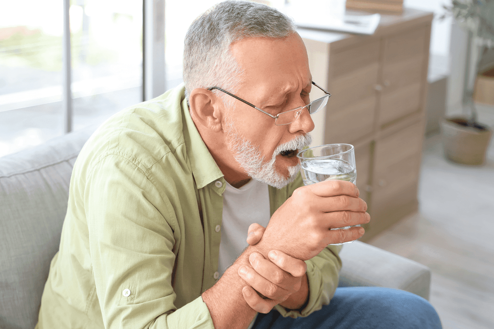 An older man struggles to hold a glass of water, showing signs of hand weakness or tremor