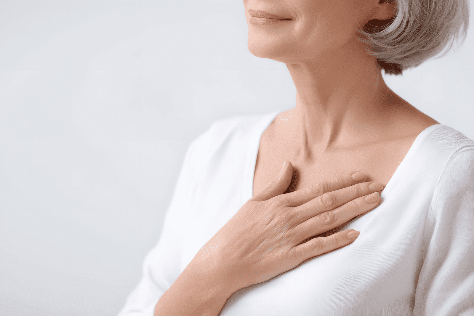 An older woman placing her hand on her chest while wearing a white top