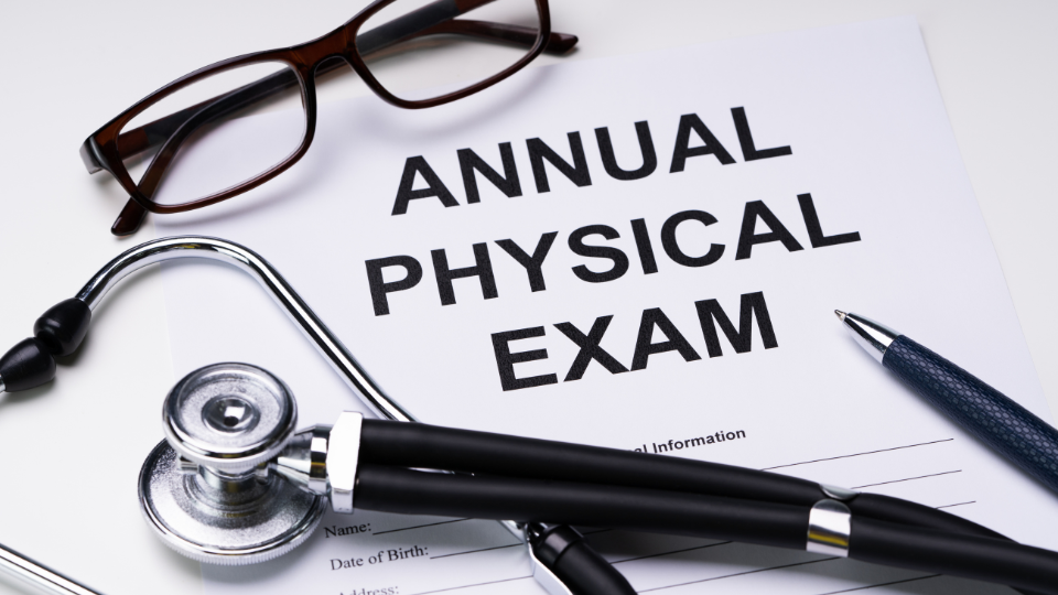 Paper saying "Annual Physical Exam" with stethoscope, glasses, and a pen on top of the paper