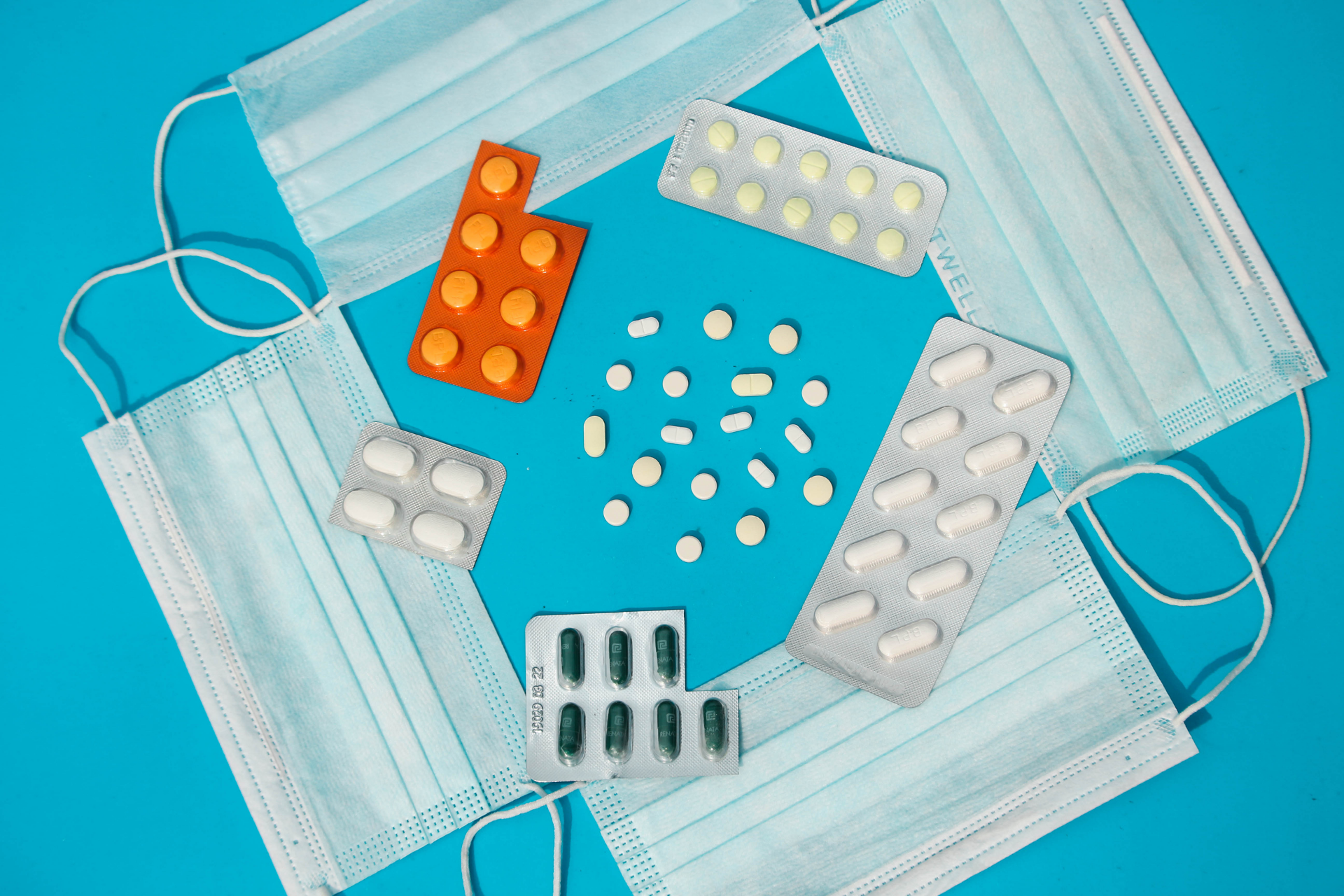 Assorted pills and blister packs arranged with face masks on a blue background