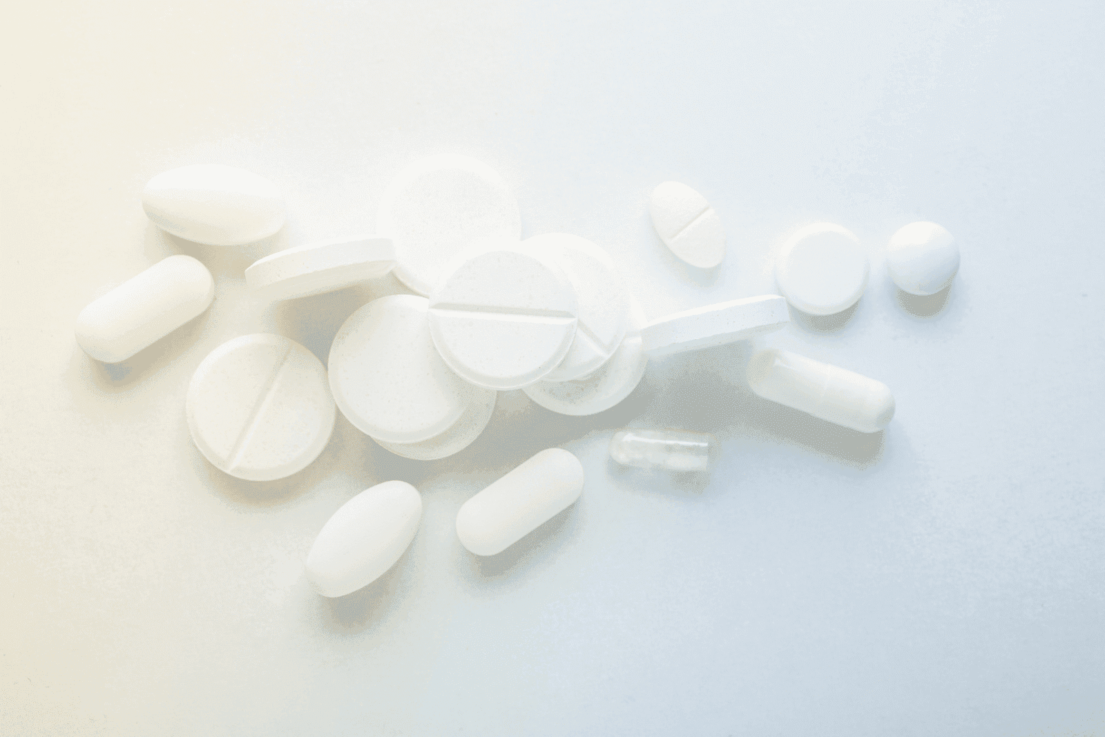 Assorted white tablets and capsules scattered on a light surface