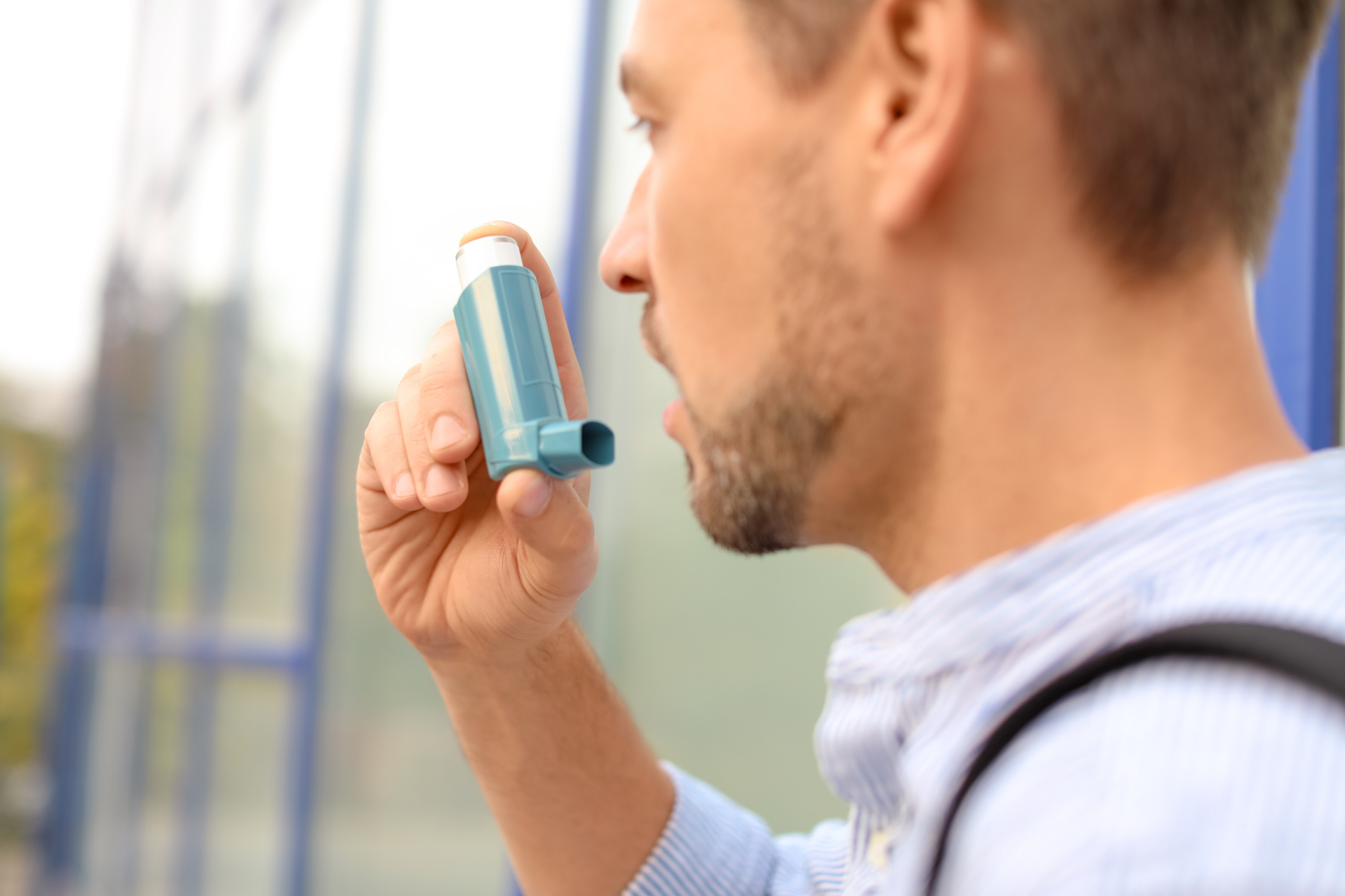 Man using a blue asthma inhaler outdoors