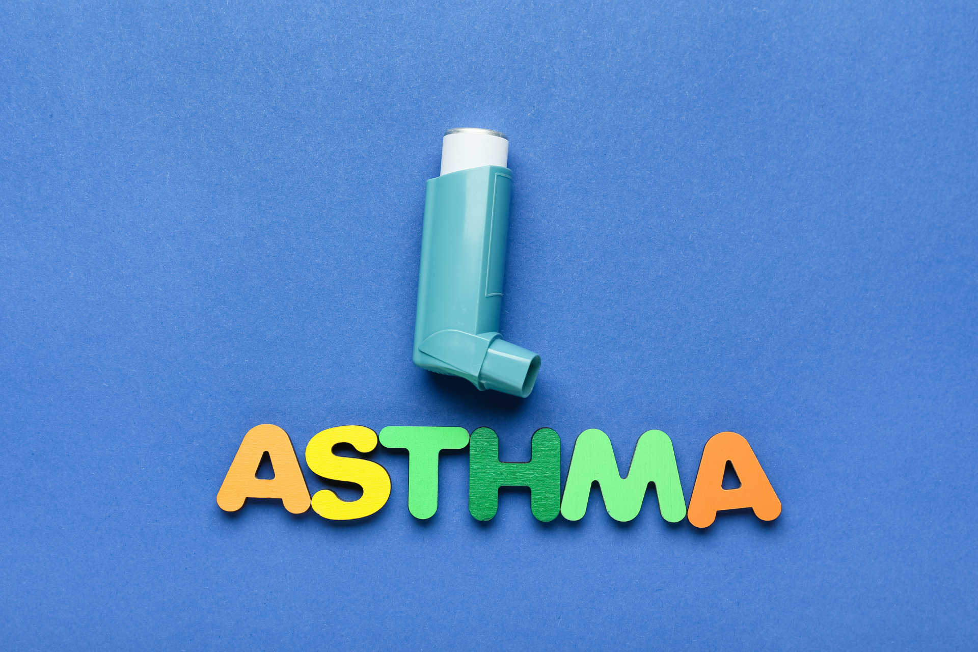 Asthma inhaler above colorful letters spelling ‘ASTHMA’ on a blue background