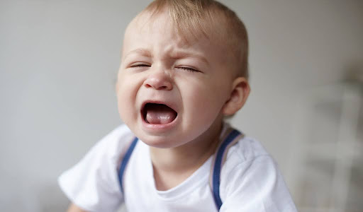 Crying baby showcasing oral thrush symptoms on the tongue.