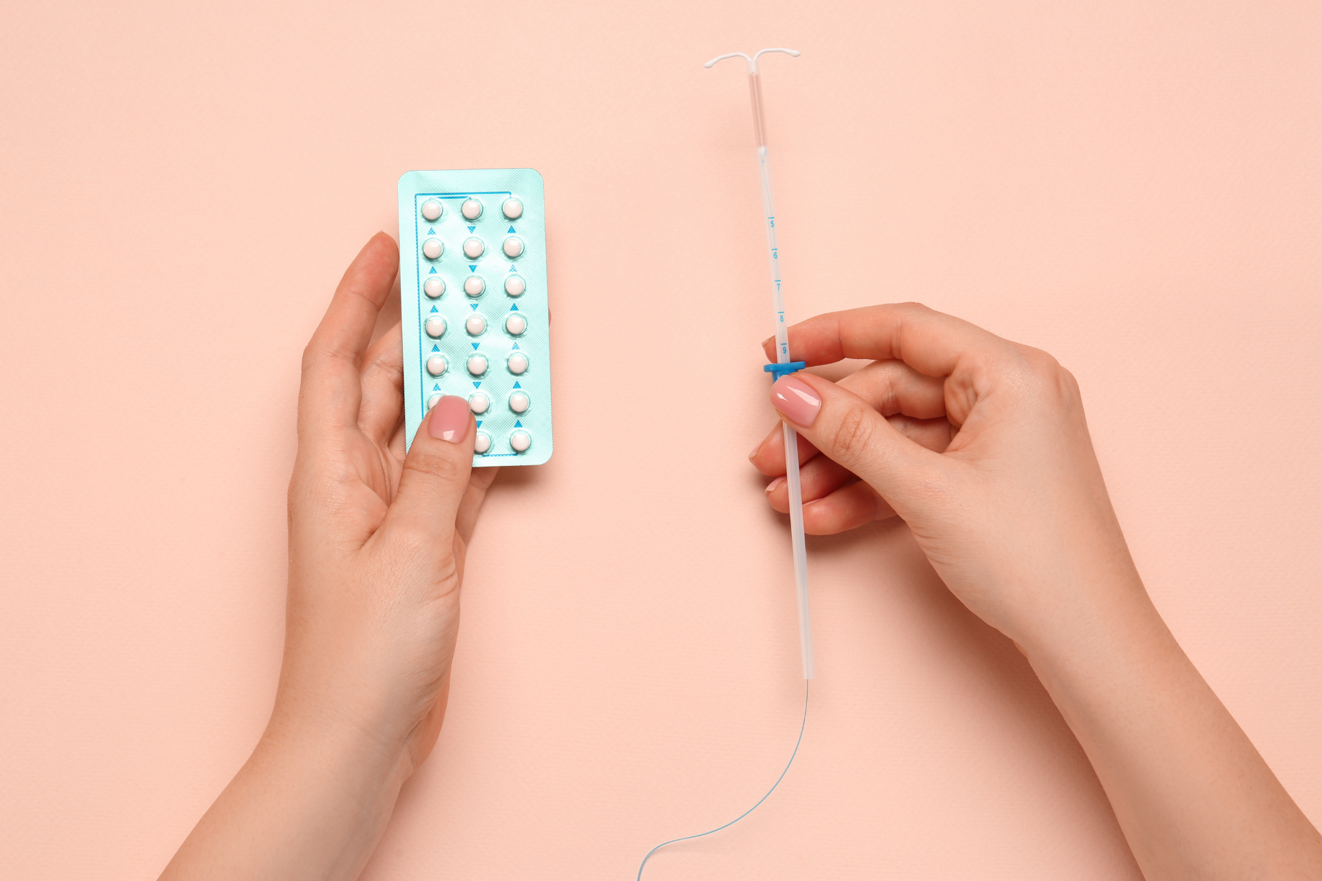 Hands holding a pack of birth control pills and an IUD on a peach-colored background