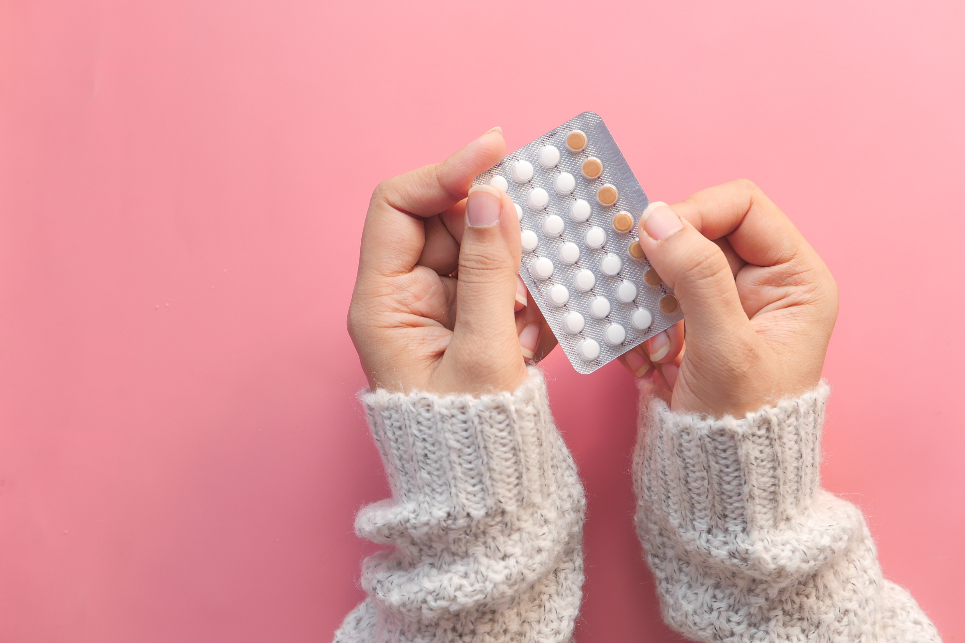 Hands holding a blister pack of oral contraceptive pills against a pink background