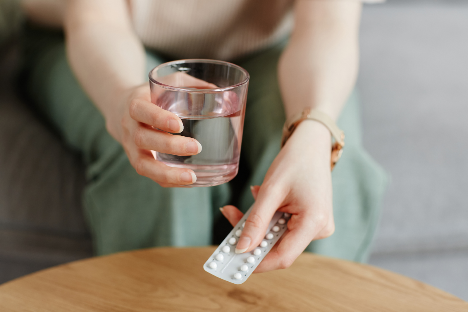 Person holding a glass of water in one hand and a blister pack of pills in the other, preparing to take medication