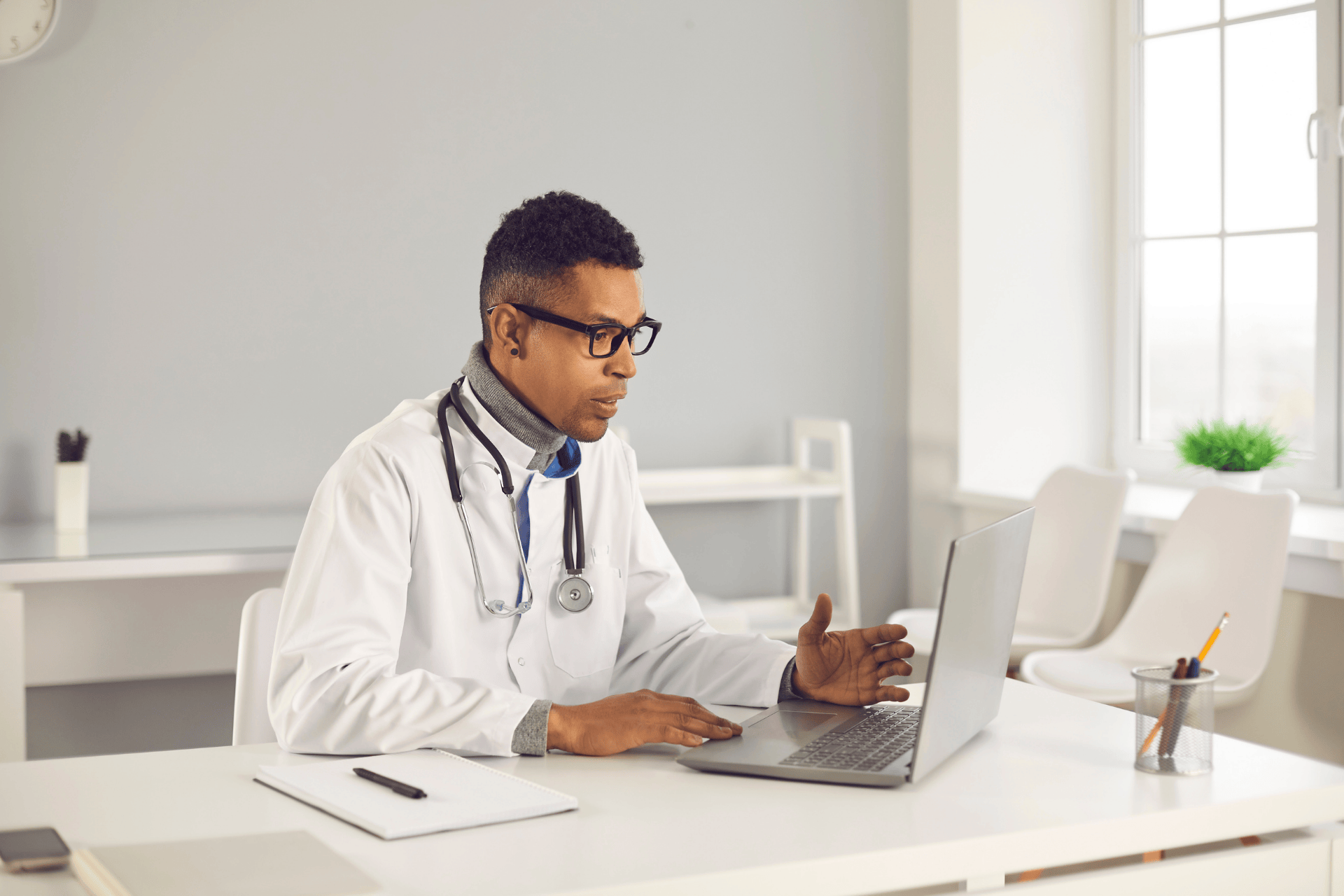 Doctor sitting at a desk, speaking while looking at a laptop during a virtual consultation.