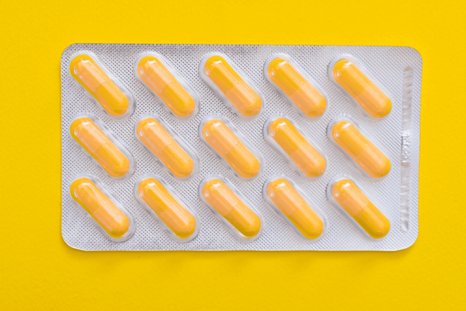 Blister pack of yellow capsules arranged in rows against a bright yellow background.