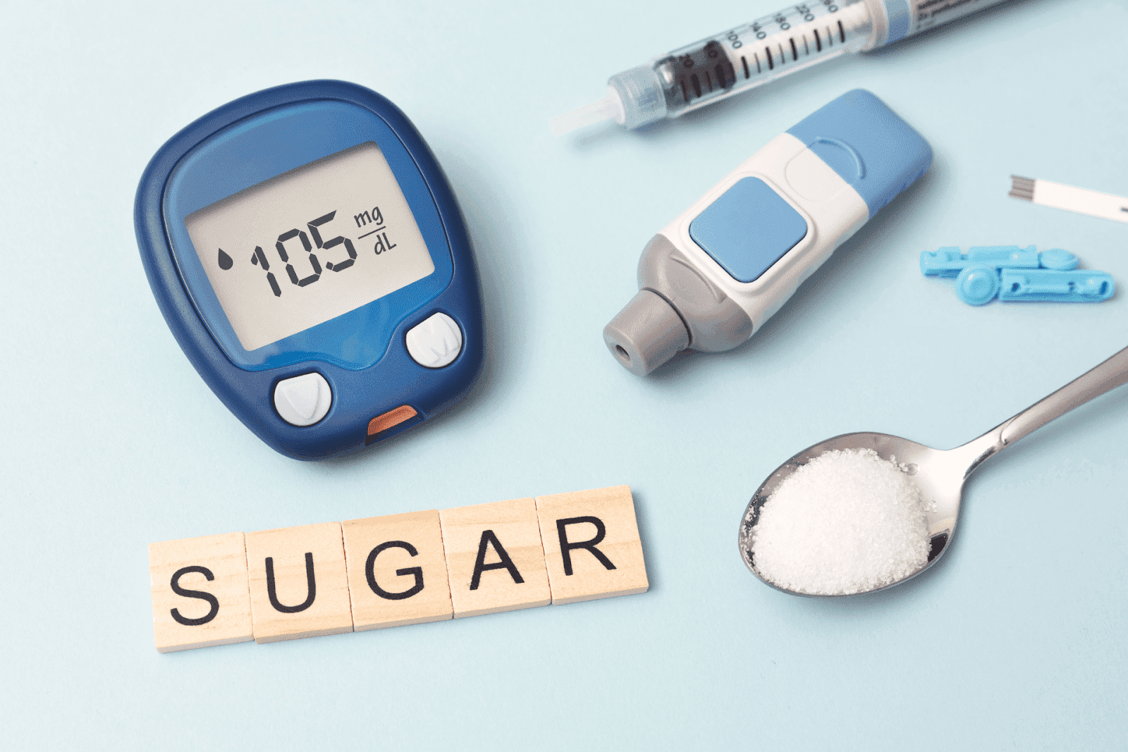 Blood glucose meter, insulin syringe, and a spoon of sugar on a light blue background.