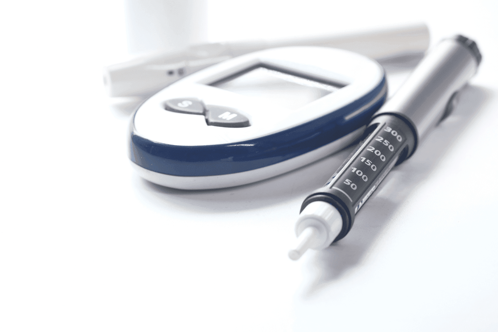 Blood glucose meter with test strip and an insulin syringe on a white background.