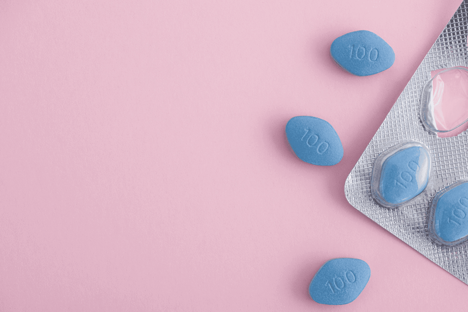 Blue tablets marked ‘100’ scattered beside a blister pack on a pink background