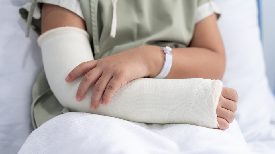 Child in hospital bed and gown holding arm with cast on