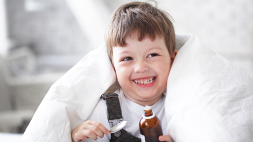 Toddler smiling while holding spoon and bottle of cough syrup
