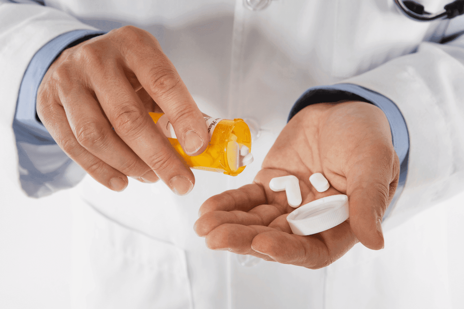 Close-up of a doctor’s hands pouring white prescription pills from an orange pill bottle