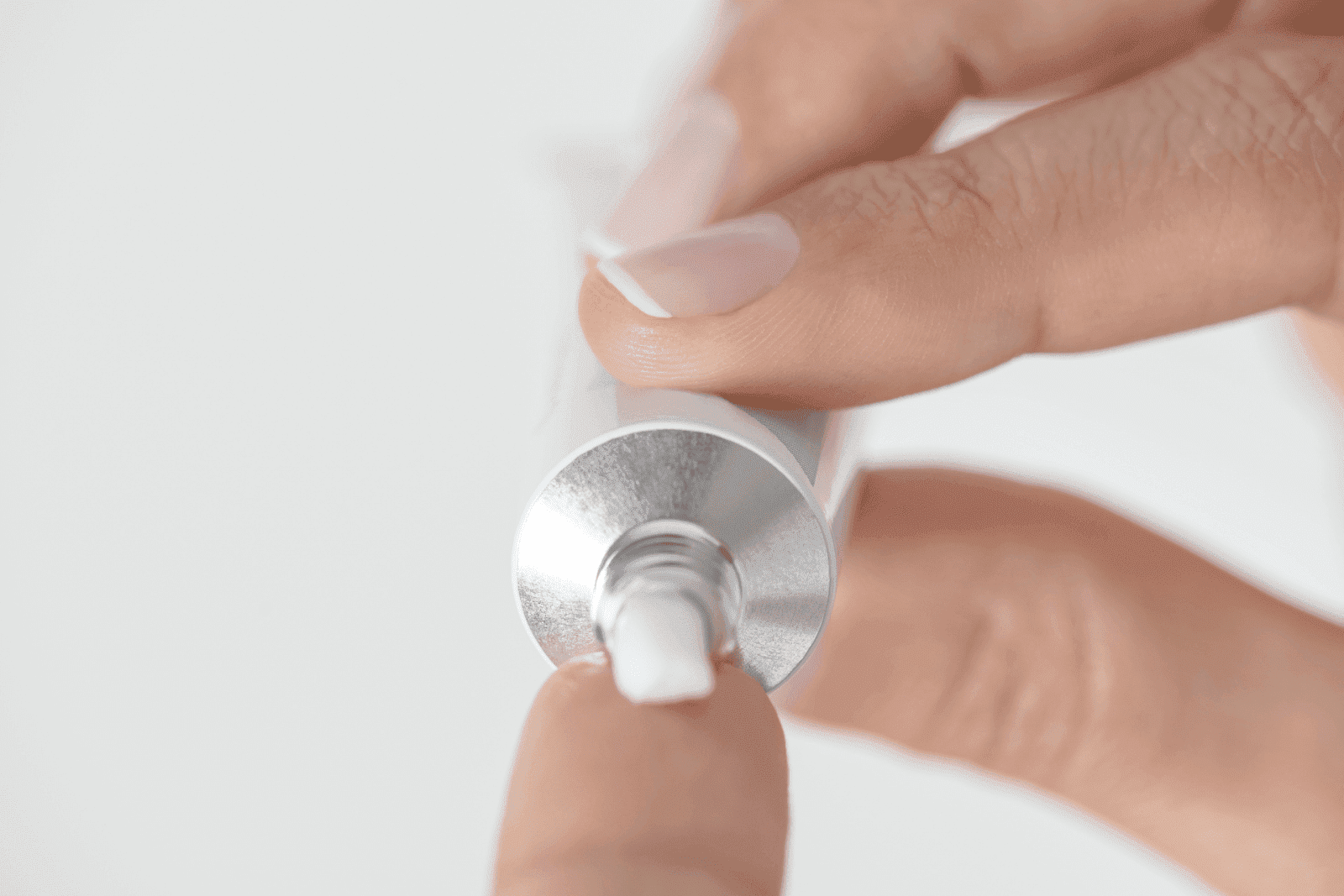 Close-up of a hand squeezing ointment from a metal tube onto a fingertip.