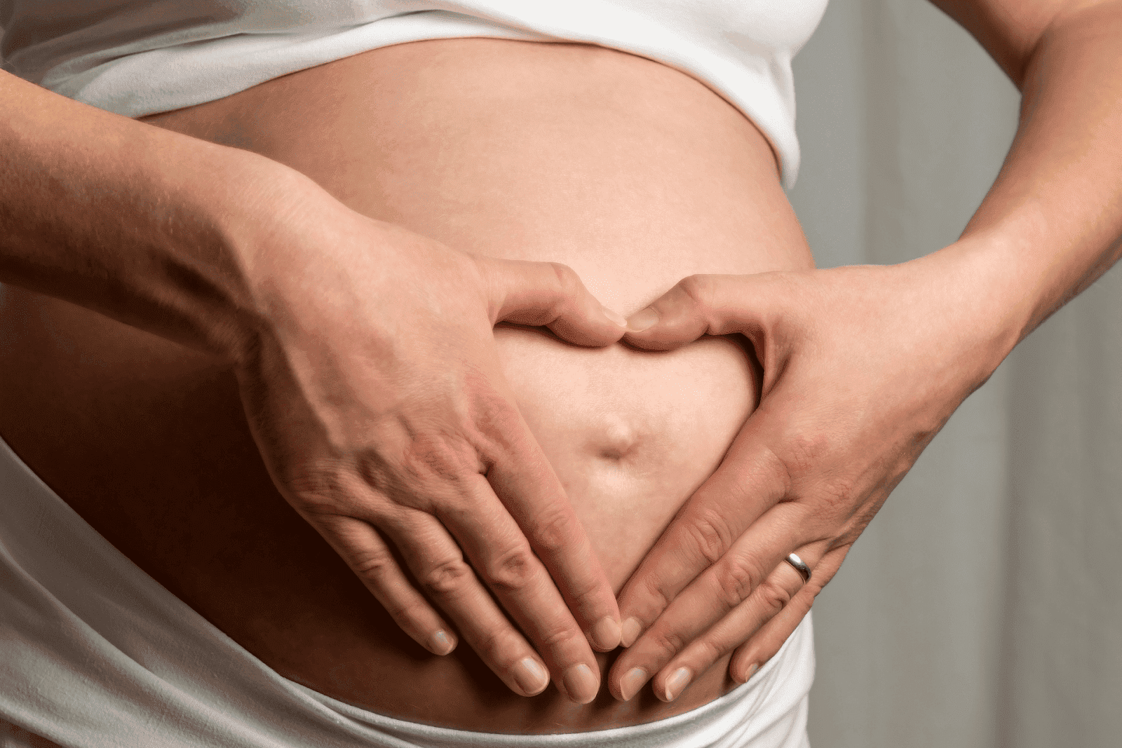 Close-up of a pregnant belly with hands forming a heart shape over it