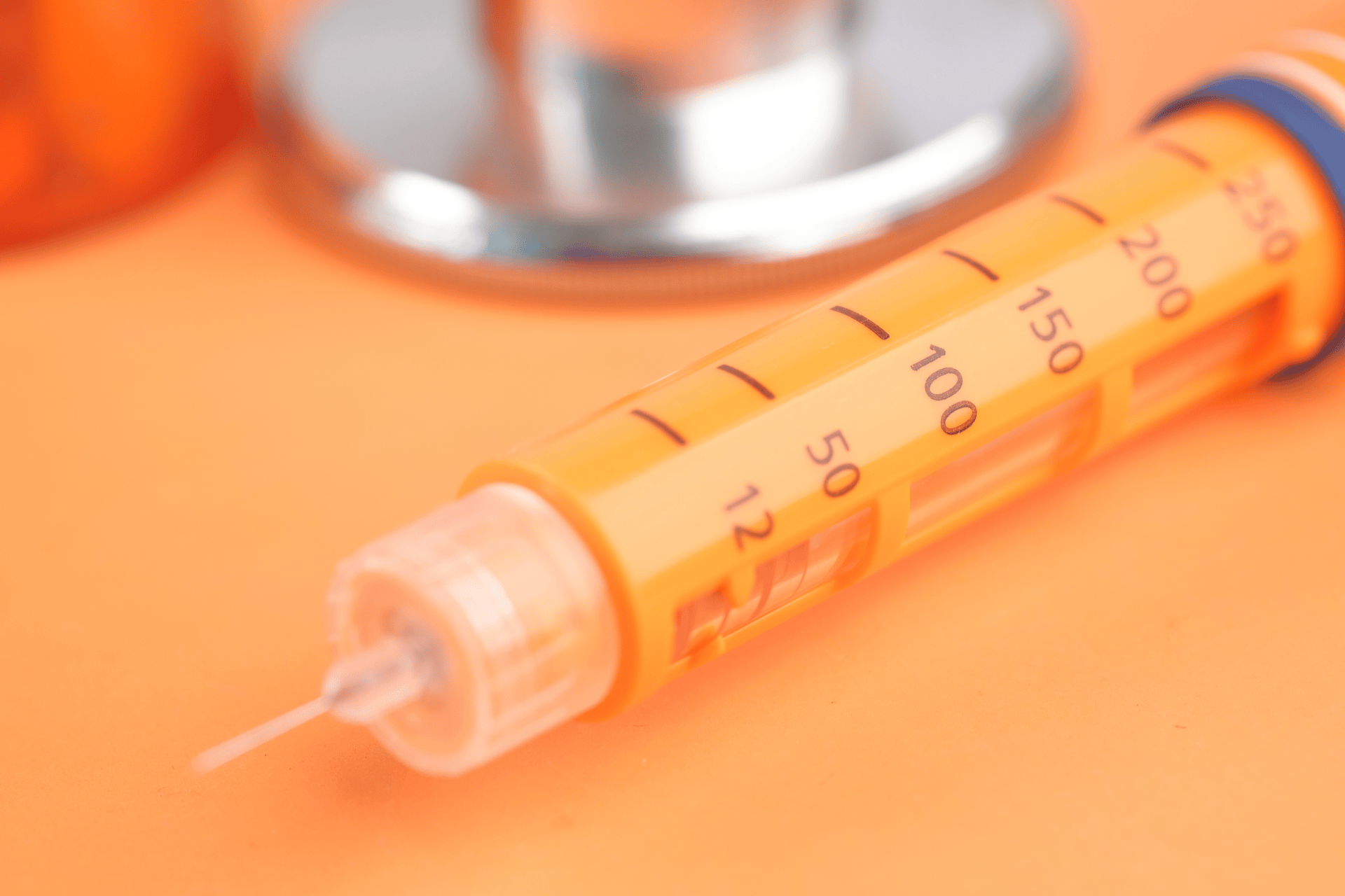Close-up of an orange insulin pen with a needle on an orange background.