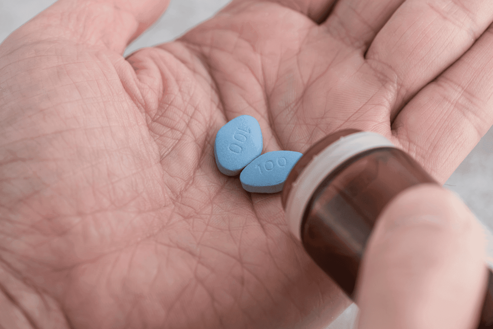 Close-up of hands holding two small blue pills and a pill bottle