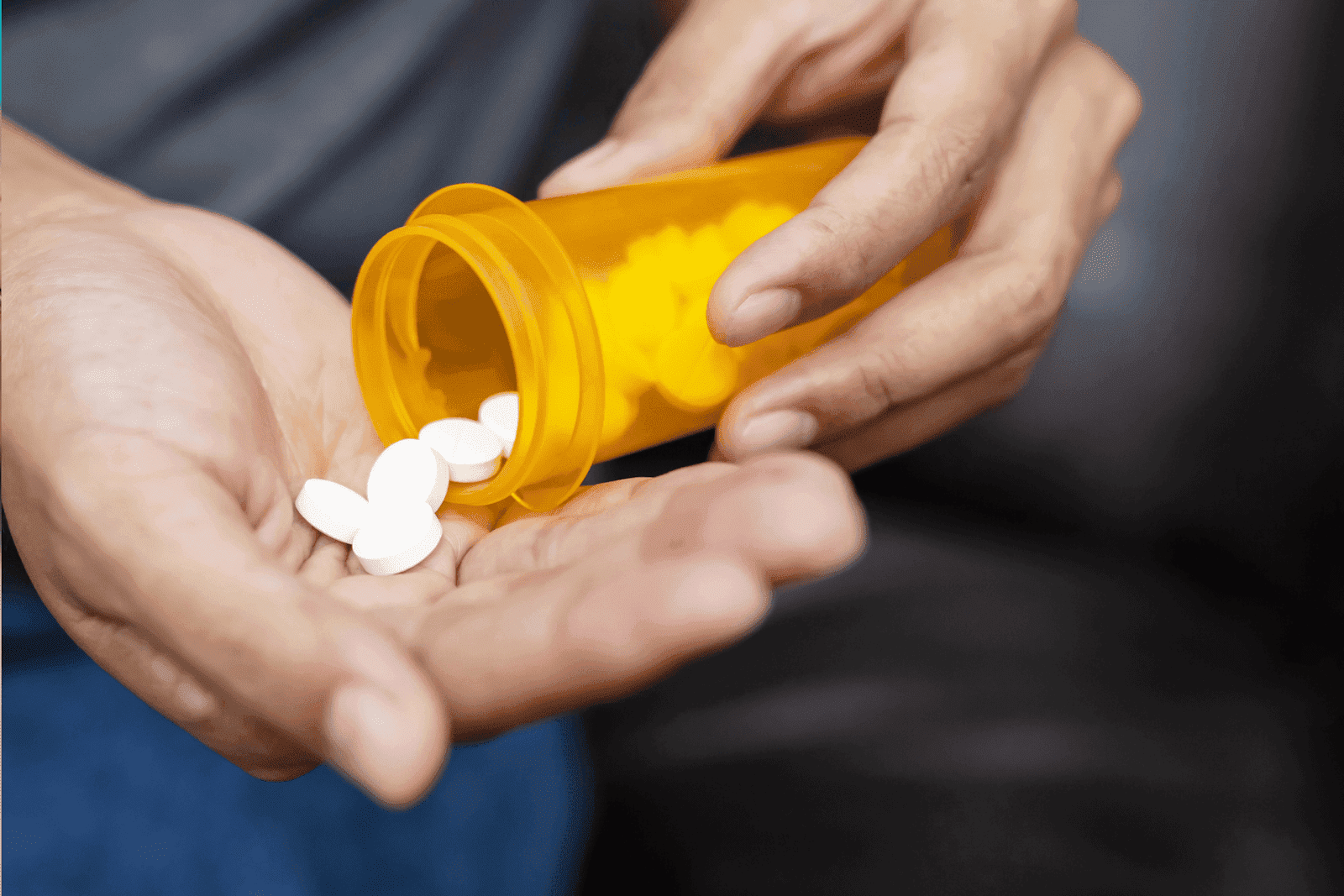 Close-up of hands pouring white tablets from a yellow prescription bottle.