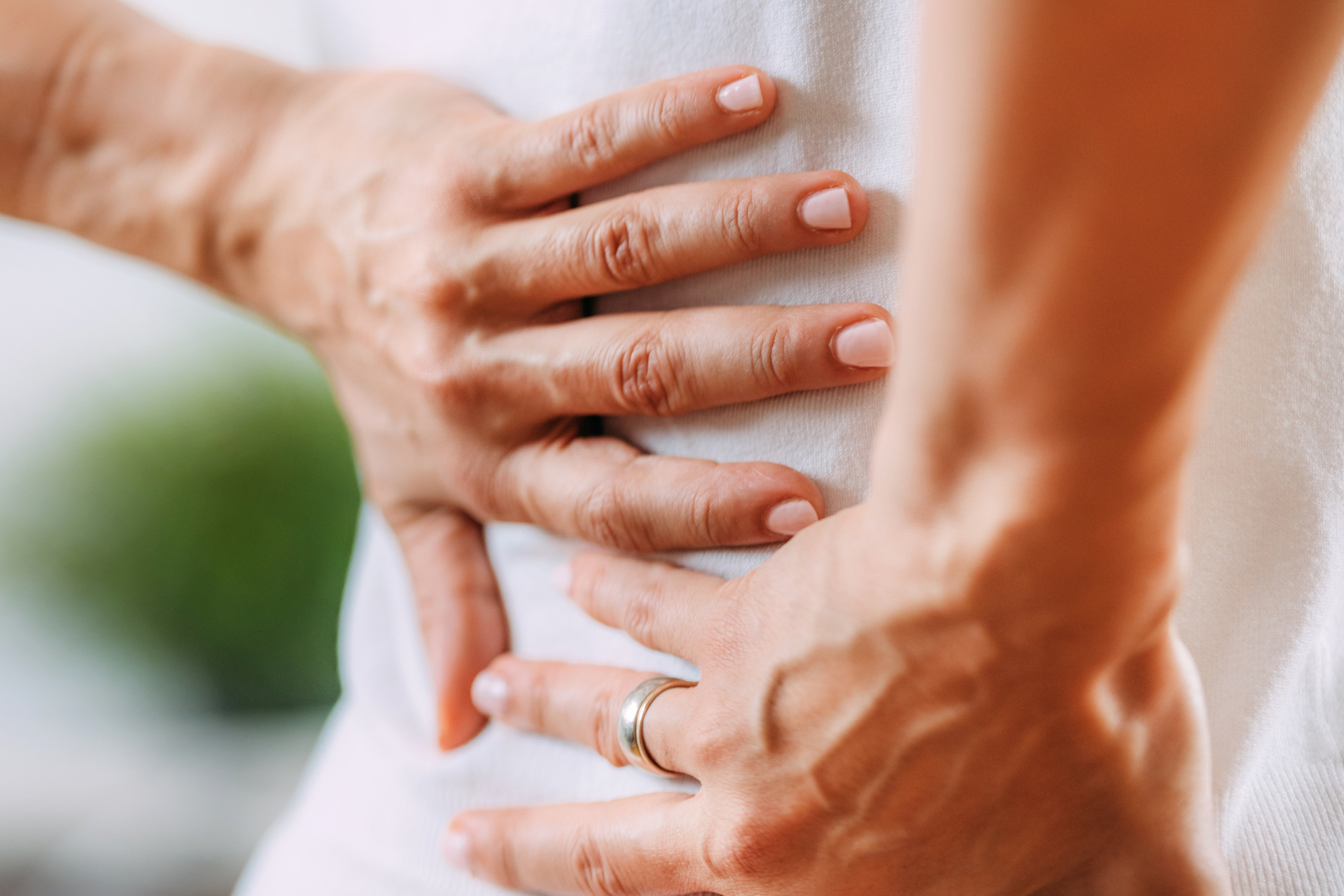 Close-up of hands pressing against the lower back, indicating back pain