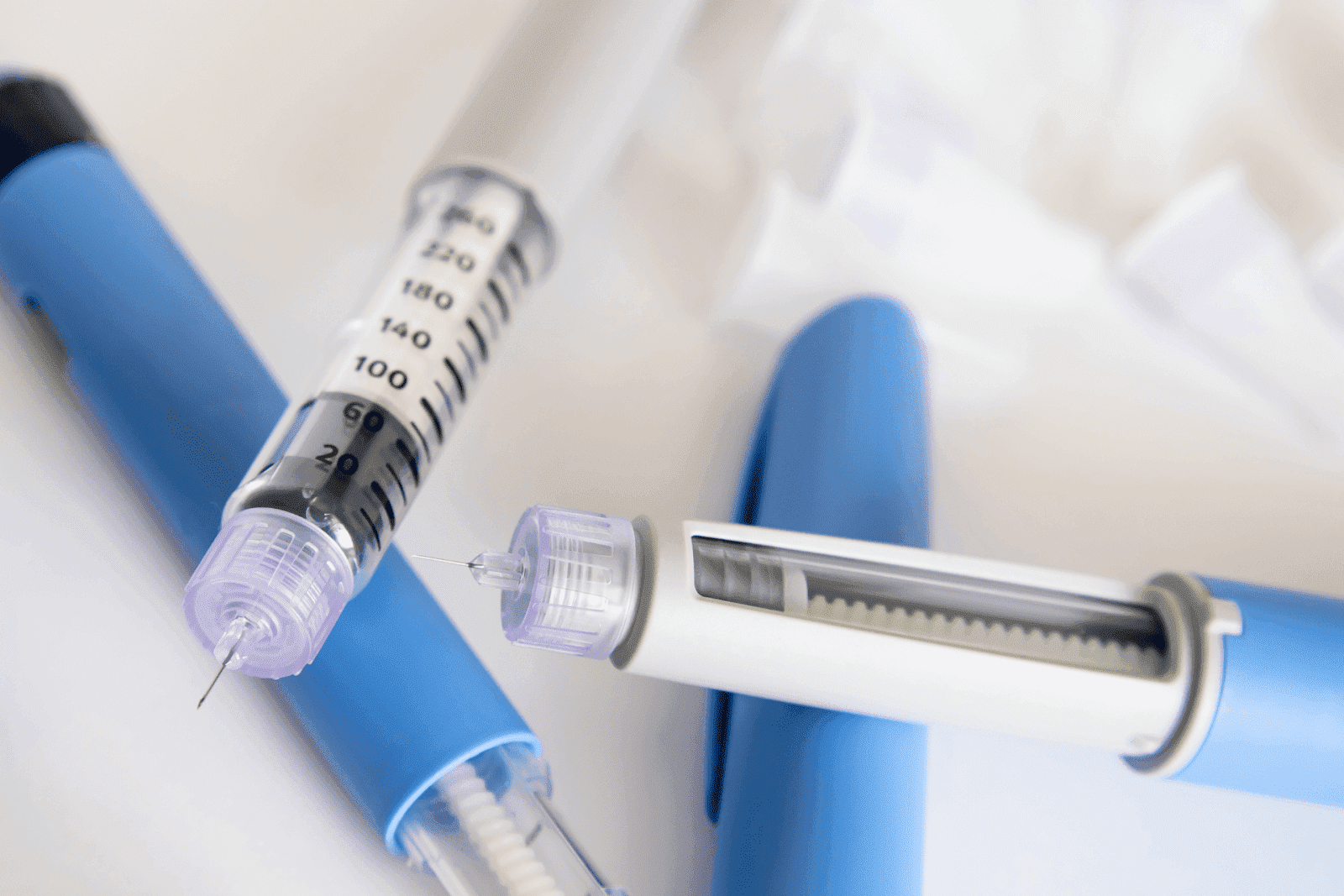 Close-up of insulin pens and needles arranged on a white surface for diabetes treatment