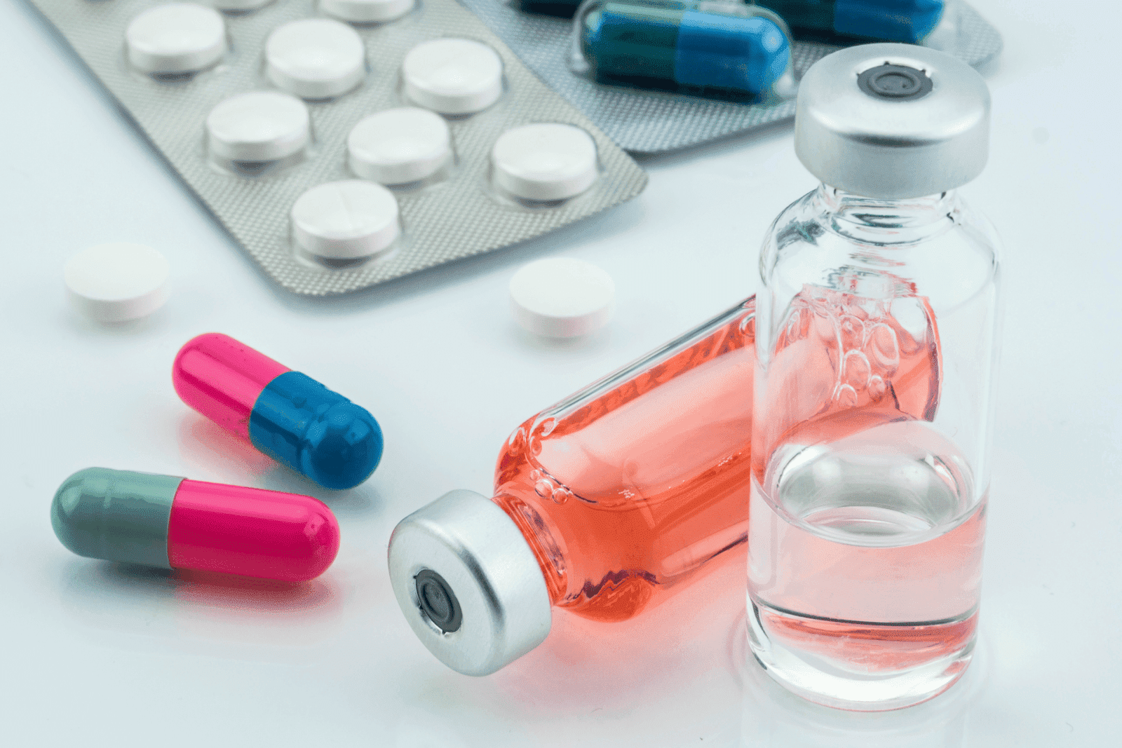 Close-up of medicine vials, capsules, and tablets arranged on a white surface