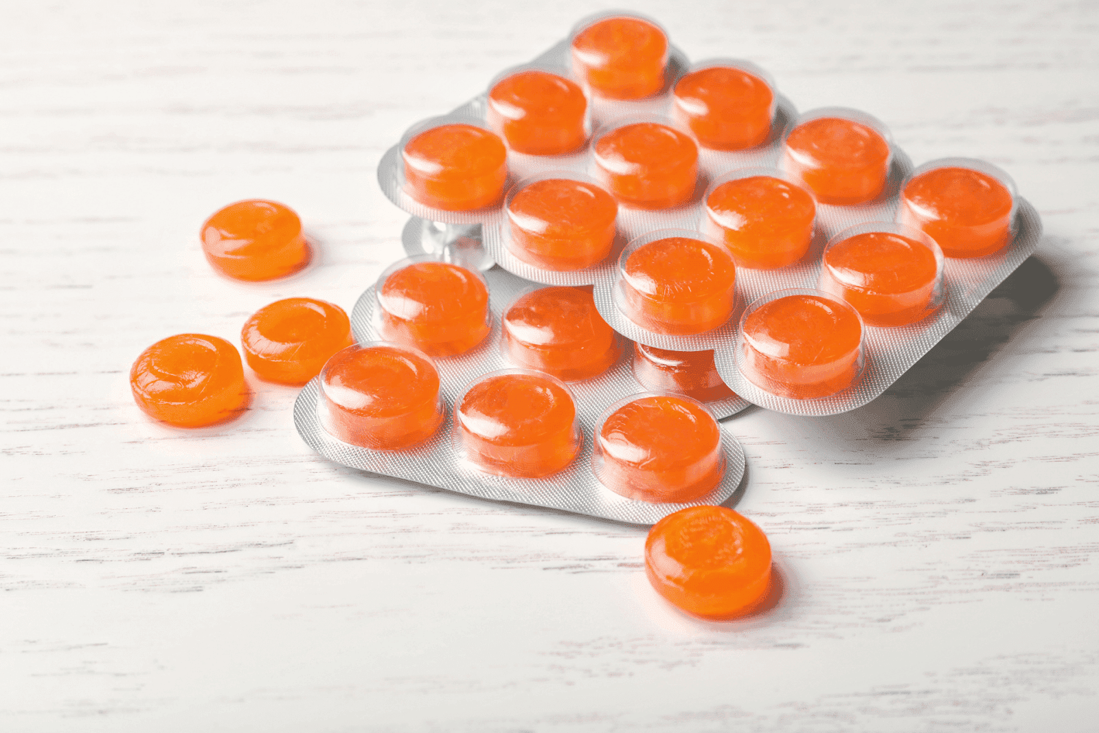 Close-up of orange throat lozenges in blister packs on a white table.