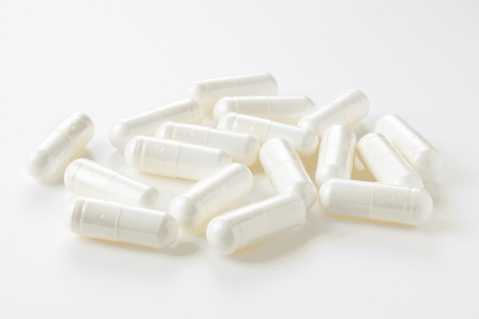 Close-up of white capsules scattered on a white surface.