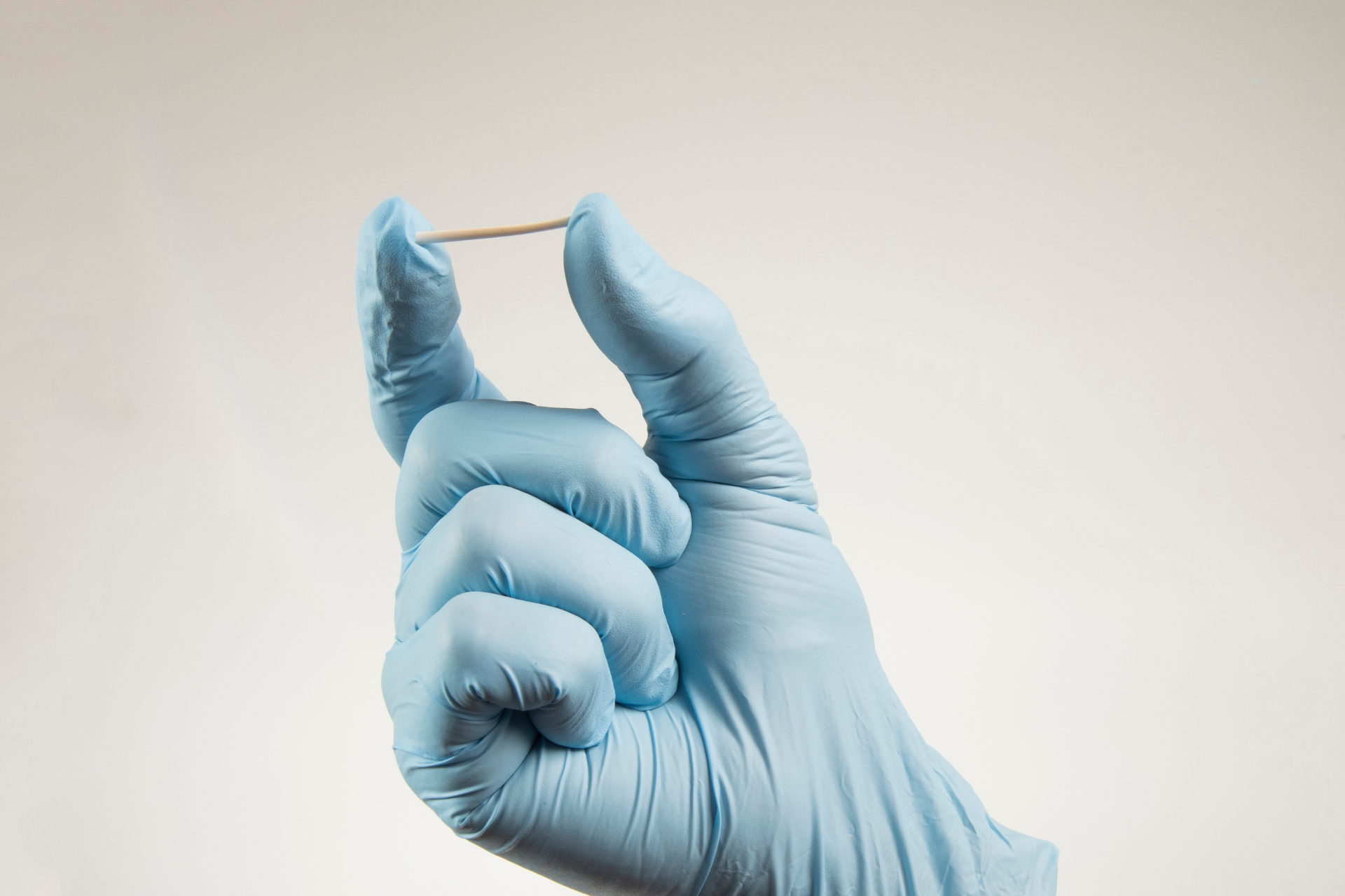 Gloved hand holding a small contraceptive implant rod between two fingers